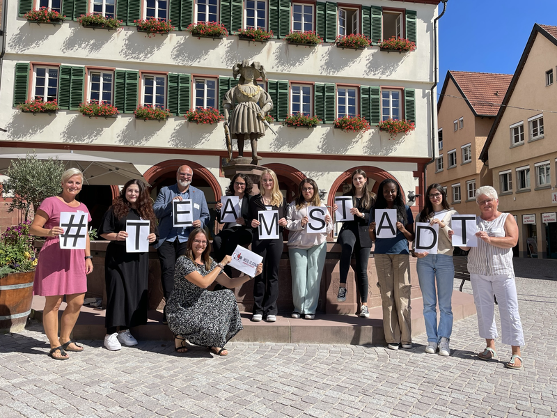 Die neuen Auszubildenden der Stadtverwaltung halten Zettel mit einzelnen Buchstaben in der Hand, die zusammen das Wort "Team Stadt" ergeben.
