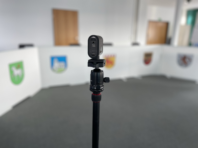Eine Videokamera steht auf einem Stativ. Im Hintergrund ist der Sitzungssaal Riquewihr. 