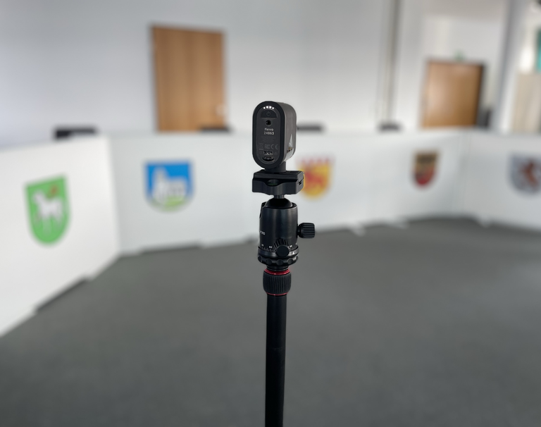 Eine Videokamera steht auf einem Stativ. Im Hintergrund ist der Sitzungssaal Riquewihr. 