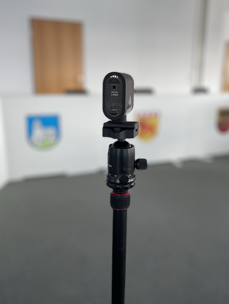 Eine Videokamera steht auf einem Stativ. Im Hintergrund ist der Sitzungssaal Riquewihr. 
