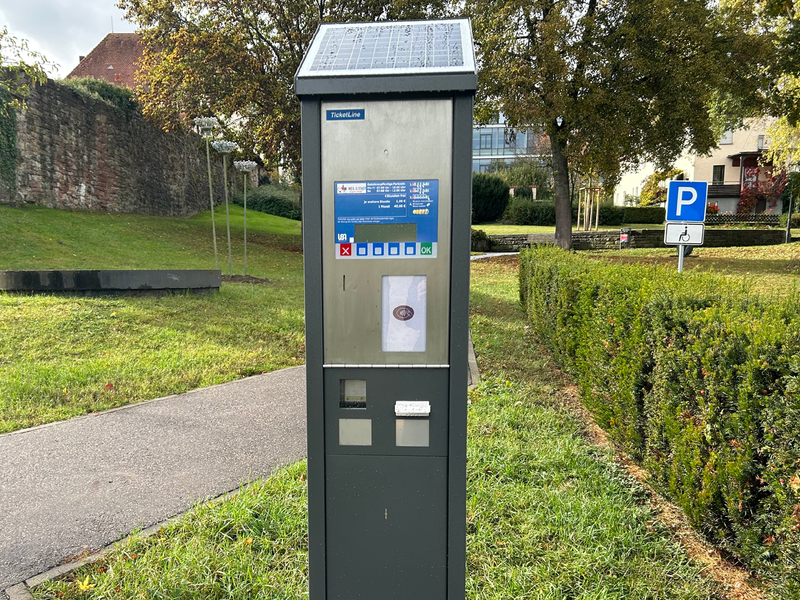 Ein Parkscheinautomat steht am Rand eines Parkplatzes.