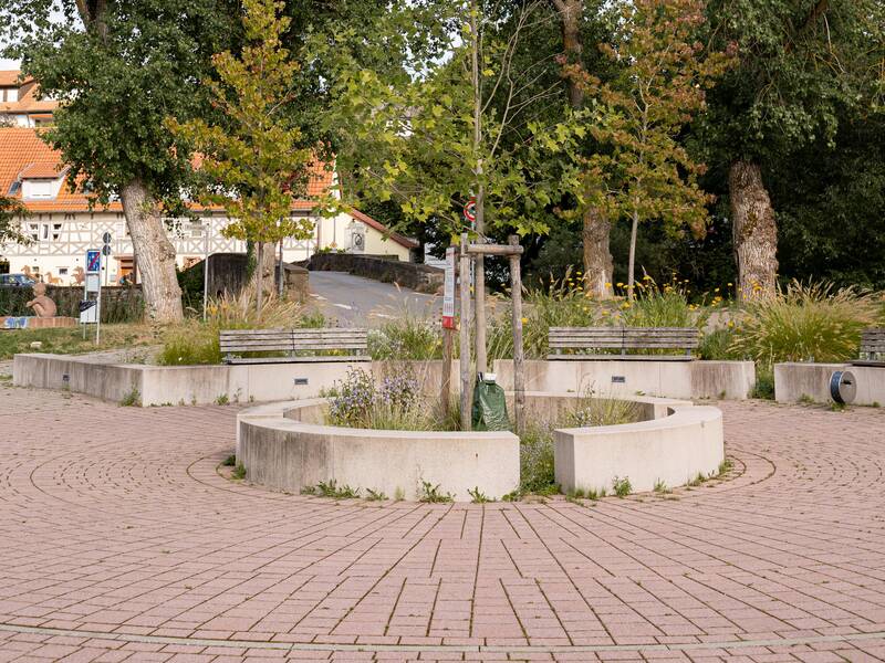 Ein kleiner Platz mit Bäumen und Sitzgelegenheiten.