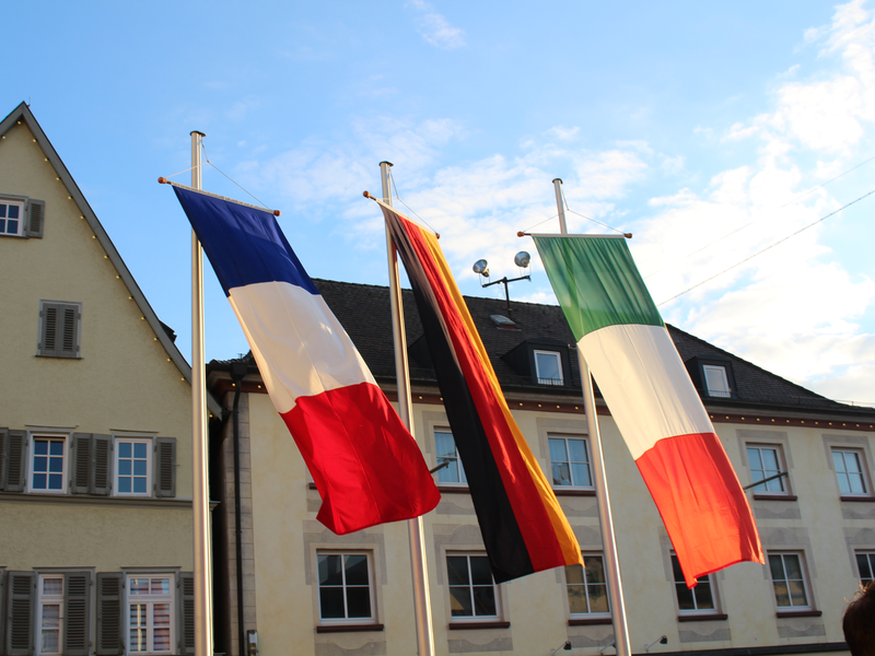 Die Flaggen von Frankreich, Deutschland und Italien wehen nebeneinander im Wind.