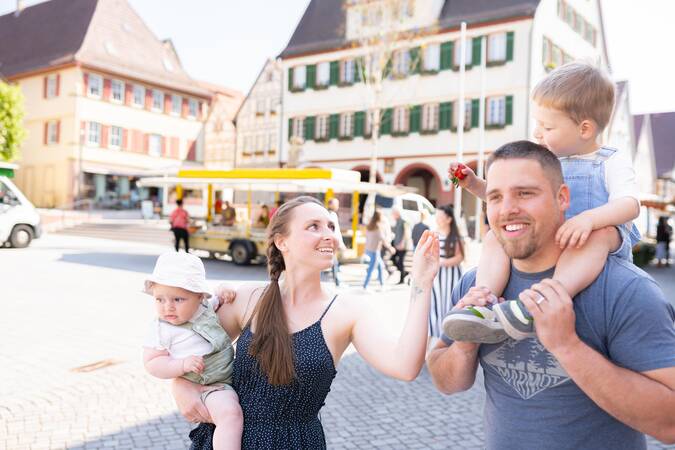 Junge Familie trägt Kinder am Wochenmarkt auf den Armen