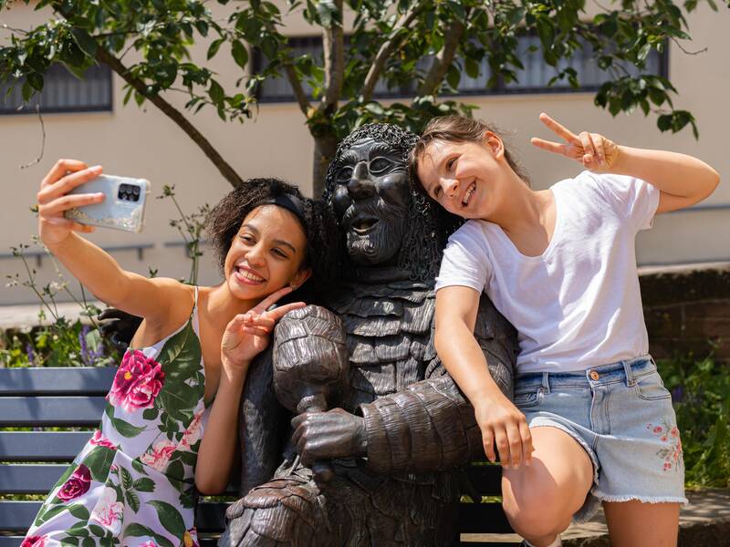 Zwei Mädchen machen ein Selfie mit der Schelmenstatue am Narrenbrunnen