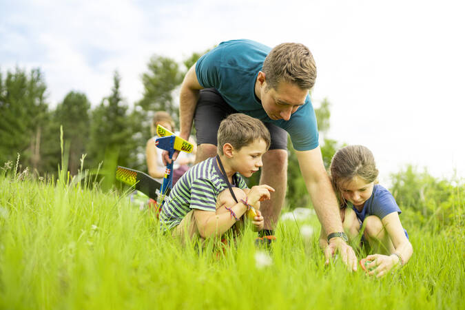 Vater der seinen Kindern etwas in der Wiese zeigt