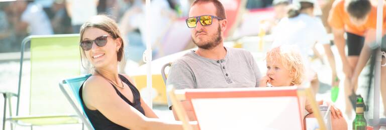 Menschen sitzen in Liegestühlen im Sand und genießen die Atmosphäre