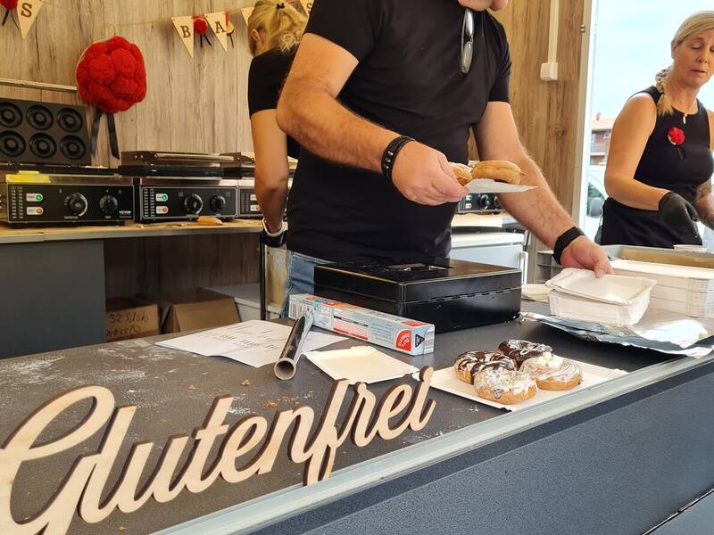 Ein Mann steht in einer Küche hinter der Theke mit der Aufschrift "Glutenfrei" und serviert Essen.