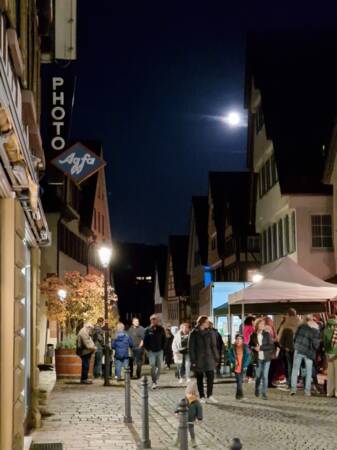 Menschen flanieren bei Nacht über Pflastersteine in historischer Altstadt