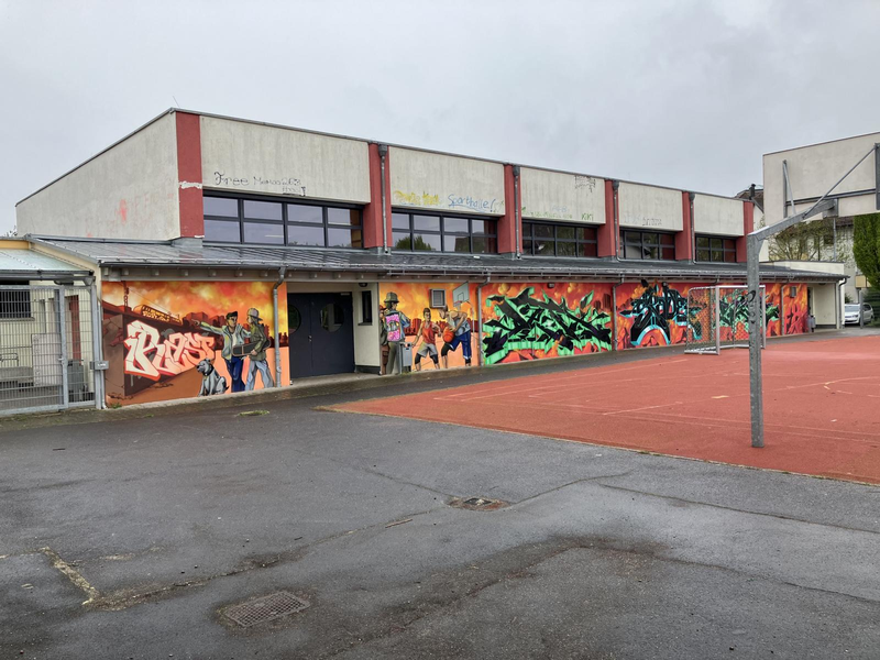 Die Stadthalle mit Grafitti an der Wand, im Vordergrund ein roter Sportplatz.