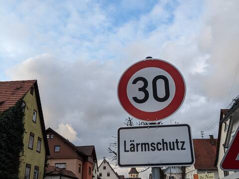 Das Verkehrszeichen "Tempo 30" sowie das Zusatzschild "Lärmschutz" steht an der Hauptstraße in Merklingen. Im Hintergrund sind die Straße, Häuser und Autos.