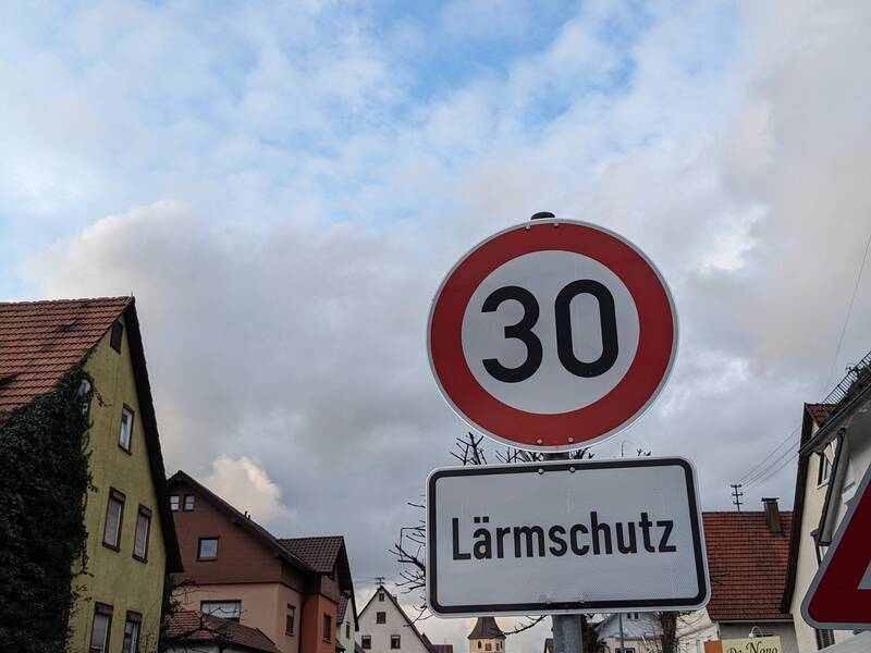 Das Verkehrszeichen "Tempo 30" sowie das Zusatzschild "Lärmschutz" steht an der Hauptstraße in Merklingen. Im Hintergrund sind die Straße, Häuser und Autos.