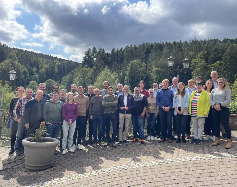 Die Mitglieder des Gemeinderates, die Verwaltungsspitze und die Amtsleiter stehen zusammen. Im Hintergrund ist Wald. 