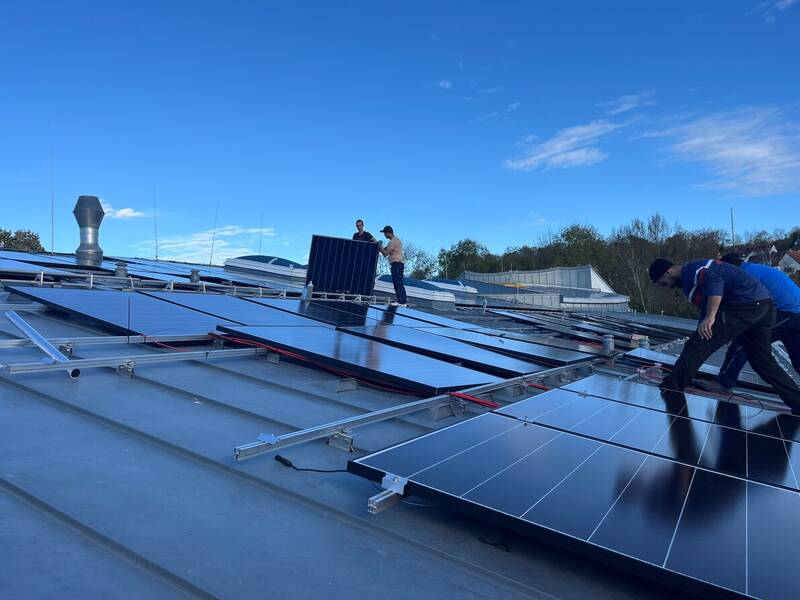 Mehrere Personen installieren Solarzellen auf einem Dach unter klarem, blauem Himmel.