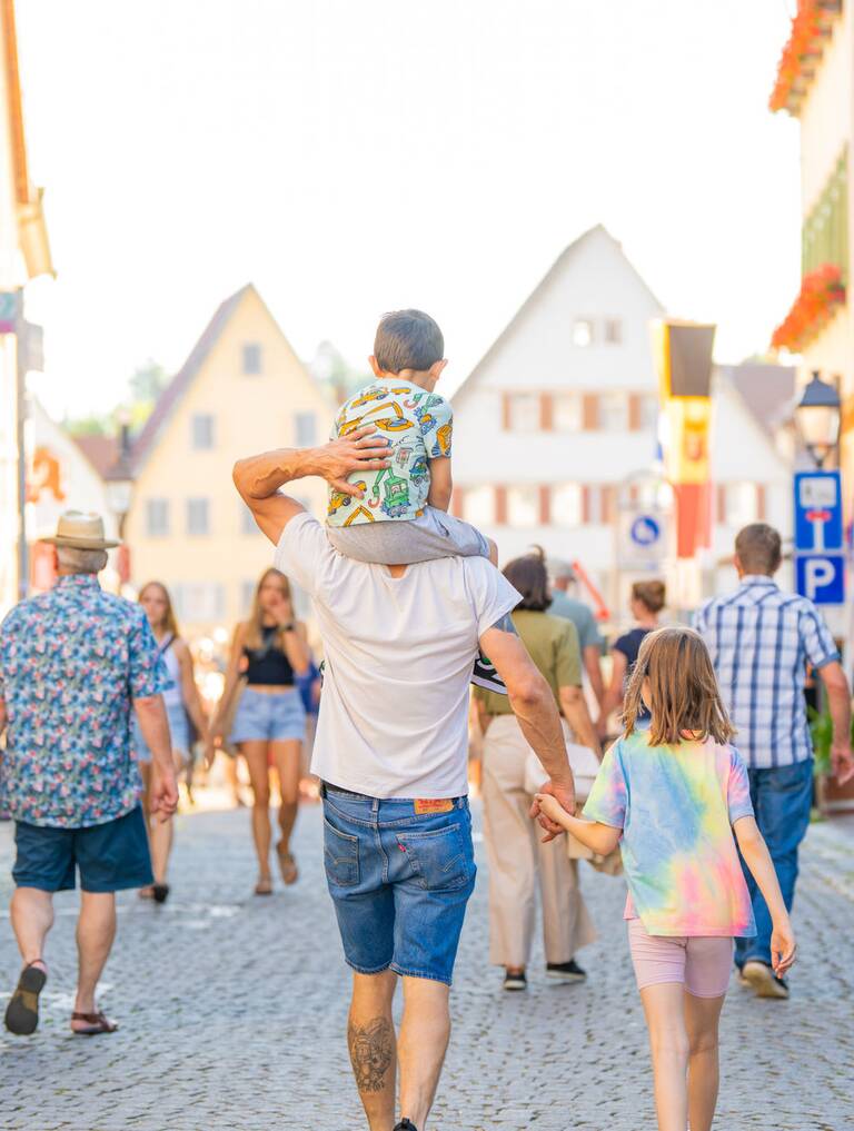 Eine belebte, sonnige Fußgängerstraße in der Altstadt von Weil der Stadt mit Menschen, die spazieren und Geschäfte auf beiden Seiten.