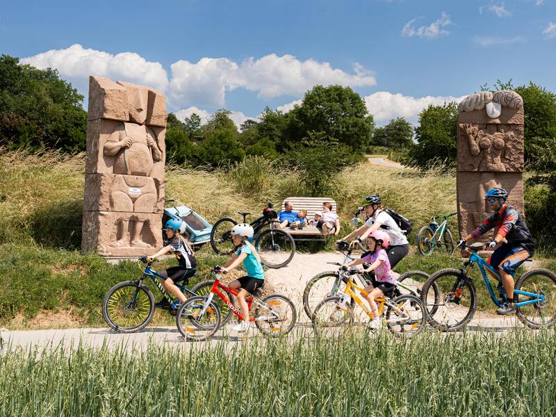 Radfahrer auf dem Sculptoura Radweg fahren an einem Rastplatz vorbei.