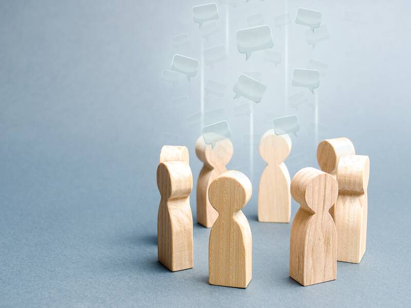 Mehrere Holzfiguren stehen in einem Kreis. Die Sprechblasen über den Figuren zeigen, dass sie miteinander kommunizieren.
