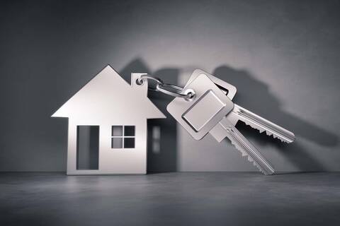 An einem Schlüssel hängt als Schlüsselanhänger ein Haus aus Metall.