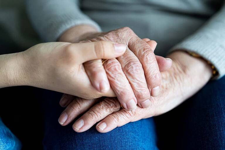 Eine junge Person hält die Hände von einer älteren Person.