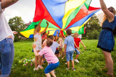 Kinder spielen beim Sommerferienprogramm mit einem Regenbogenzelt in der freien Natur.
