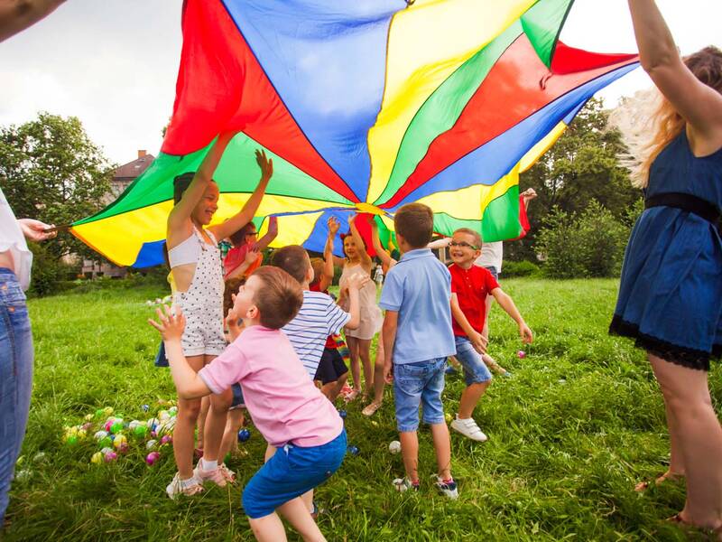 Kinder spielen beim Sommerferienprogramm mit einem Regenbogenzelt in der freien Natur.
