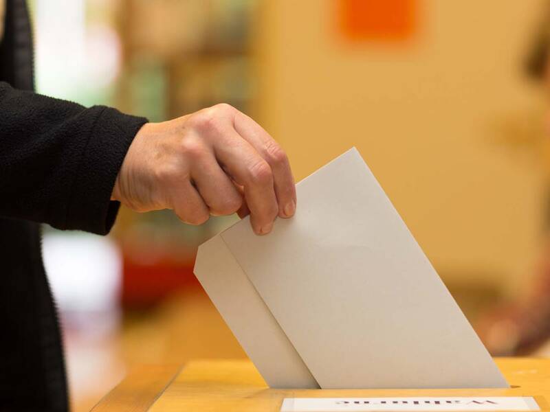 Eine Person wirft einen Umschlag in eine Wahlurne.