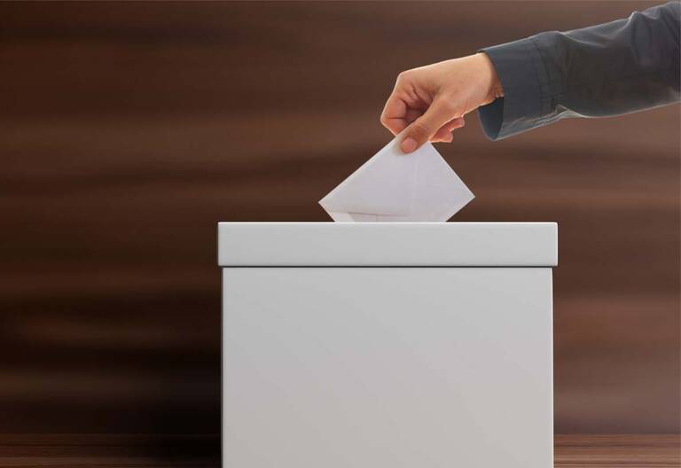 Eine Person wirft einen Umschlag in eine Wahlurne.