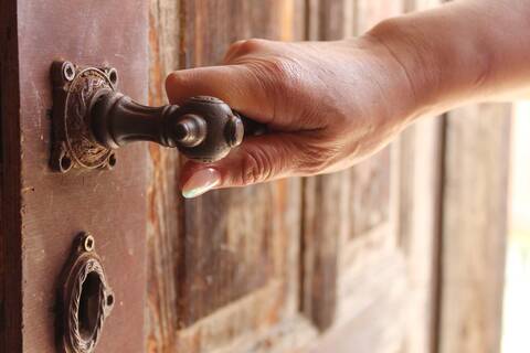 Eine Hand, die den Griff einer alten Holztür hält.
