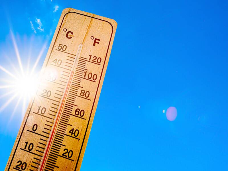 Ein Thermometer im Vordergrund zeigt hohe Temperaturen an, während die Sonne am blauen Himmel strahlt.
