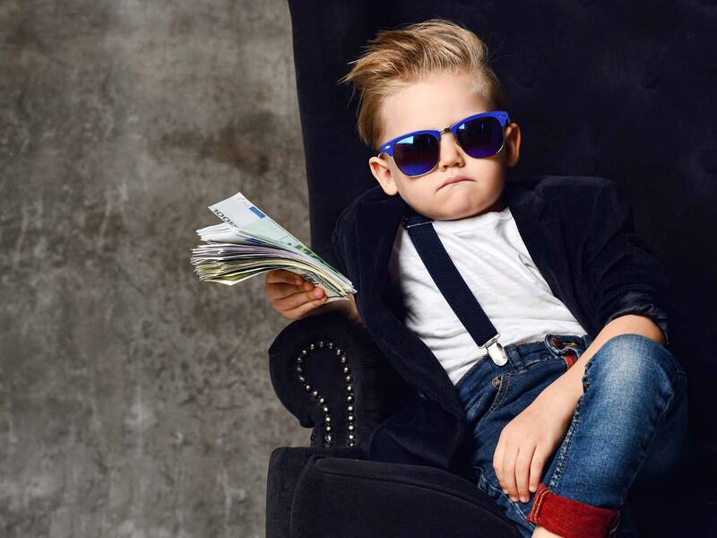 Ein gestyltes Kind mit Sonnenbrille hat viele Geldscheine in der Hand.