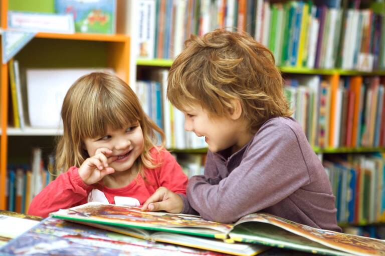 Zwei Kinder lesen Bücher in einer Bücherei.