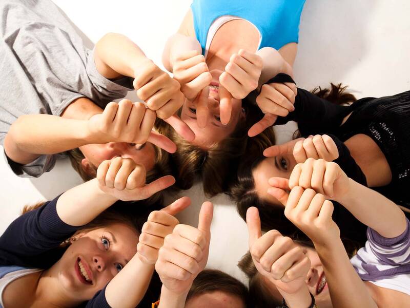 Viele junge Menschen liegen im Kreis auf dem Rücken und zeigen ihren Daumen nach oben.