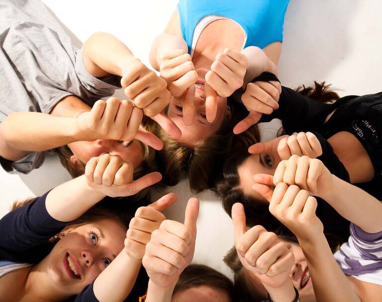 Viele junge Menschen liegen im Kreis auf dem Rücken und zeigen ihren Daumen nach oben.