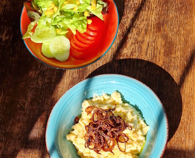 In dem blauen Teller befinden sich Käsespätzle und in dem roten Teller befindet sich ein gemischter Salat. 