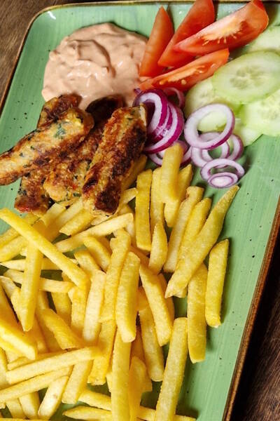 Auf dem Teller werden Pommes mit Falafelsticks und Gemüse serviert. 